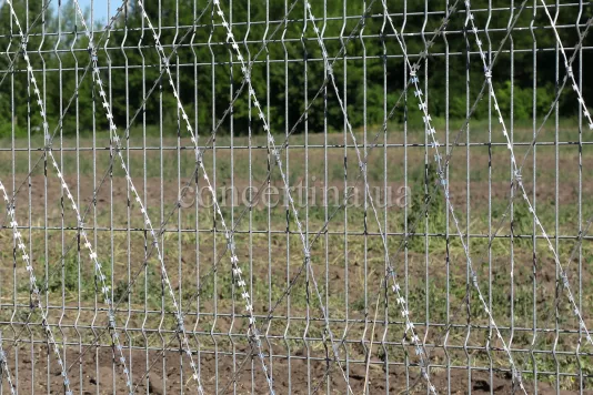 Колючая сетка Пиранья на заборе из сварных панелей